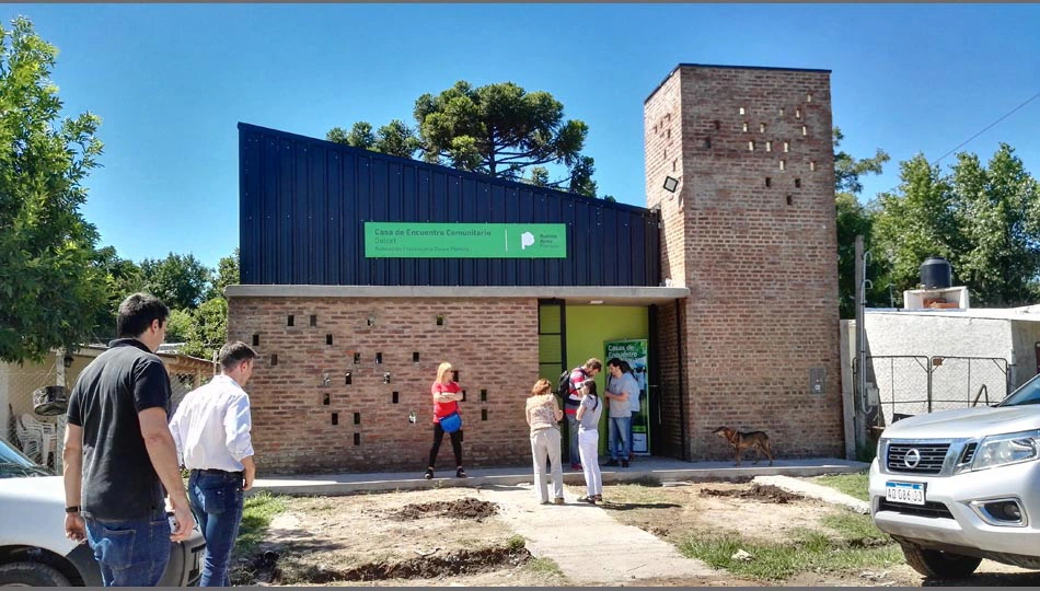 imagen de la fachada del edificio de ladrillos y chapa negra de la Casa de Encuentro Comunitario San José Obrero en La Reja Grande, Moreno, por el Estudio OUSIA Arquitectos